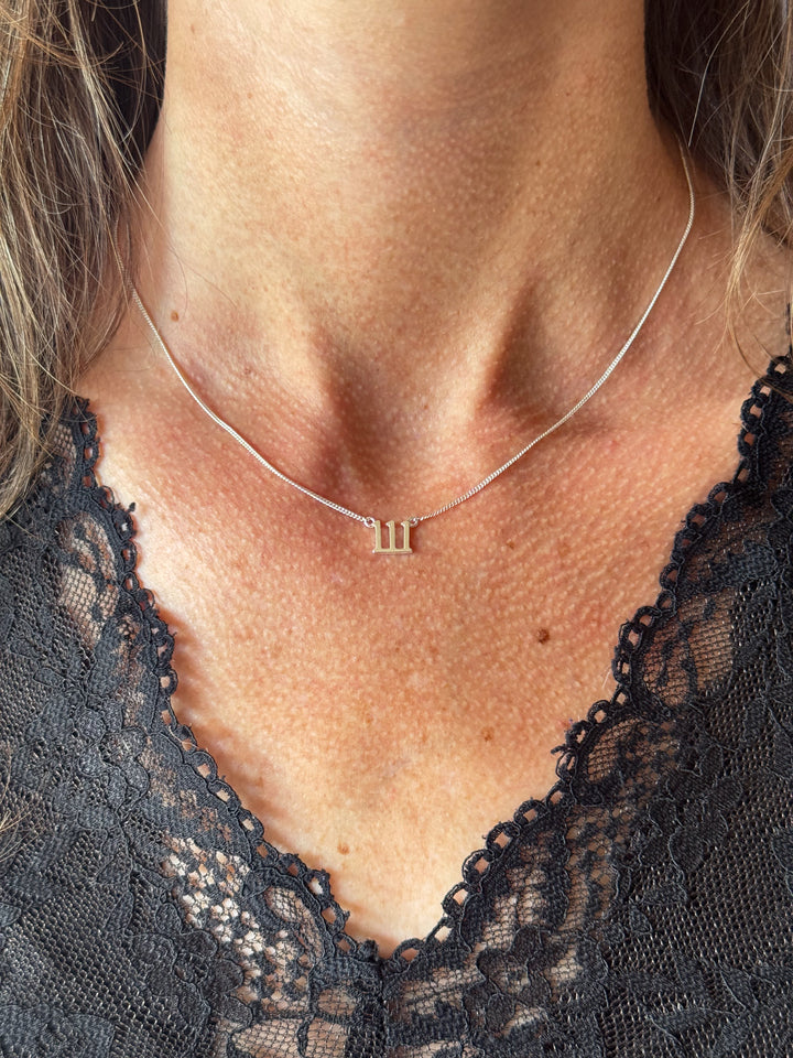 A close-up of a person's neck and chest wearing a delicate silver chain necklace with a small numeral '111' pendant, paired with a black lace top. Lucky On Purpose Jewelry Jewellery. 