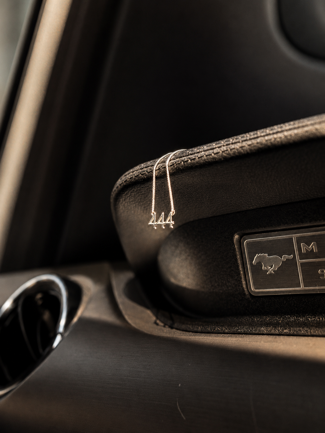A silver metal car keychain with a small dangling loop and '444' engraving, shown clipped to the leatherette armrest of a black car interior near the gear selector. Lucky On Purpose Jewelry Jewellery. 
