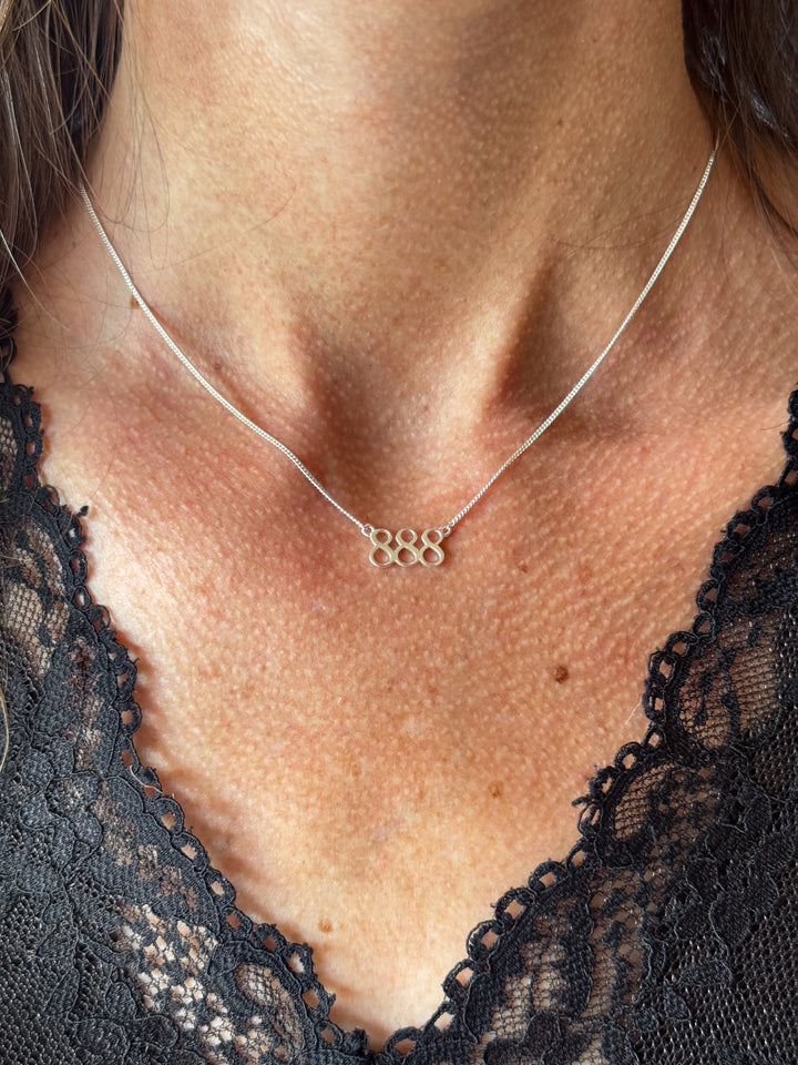 A close-up of a person's neck and chest wearing a delicate silver chain necklace with a small cluster of five interlocking circular pendant rings, paired with a black lace top. Lucky On Purpose Jewelry Jewellery. 888